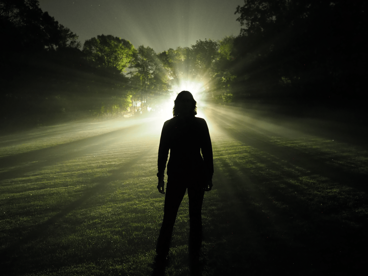 Katie Mack standing in darkness with a light shining brightly behind her